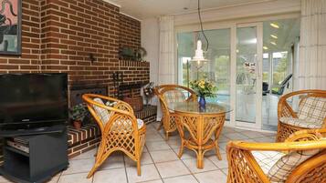 A living room with a brick fireplace, wicker furniture, a television, and a glass table.