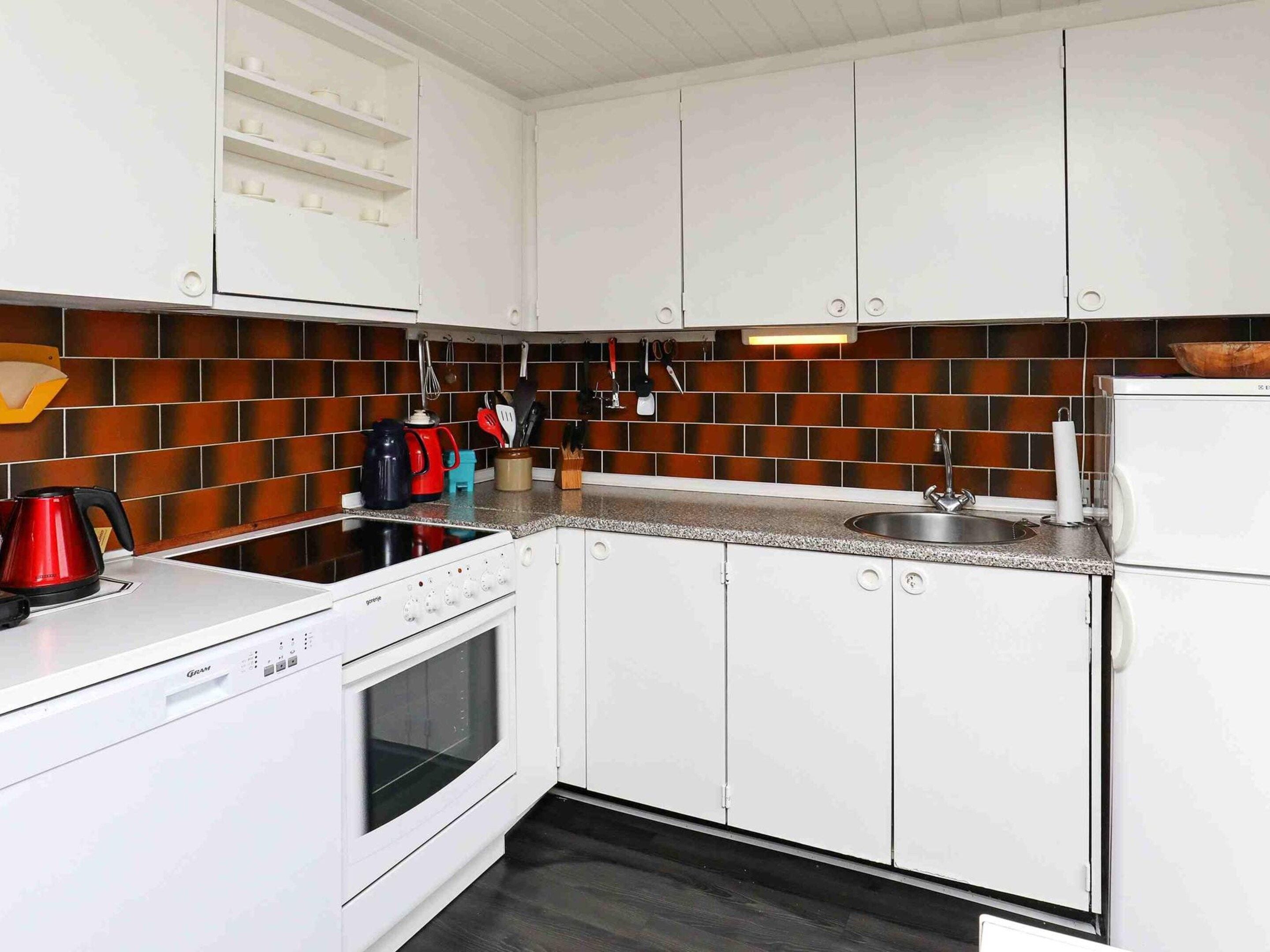 A kitchen with white cabinets, a black countertop, and a red kettle.