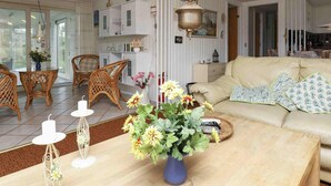 Una sala de estar con sofá, sillas de mimbre, una mesa de comedor con sillas, una lámpara colgante y un florero con flores.