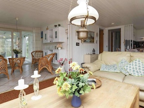 Un salon comprenant un canapé, des fauteuils en osier, une table à manger avec des chaises, une lampe suspendue et un vase rempli de fleurs.