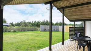 Un espacio exterior cubierto con una terraza de madera, una mesa con sillas y vistas a un jardín.