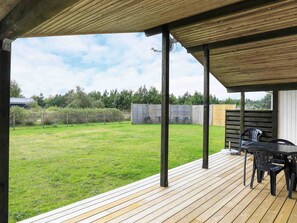 Un espace extĂ©rieur abritĂ©, dotĂ© dâune terrasse en bois, dâune table avec des chaises et offrant une vue sur une pelouse.