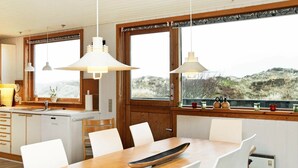 A modern kitchen with white cabinetry, a wooden dining table, and pendant lights. - Cozy Holiday Home in Oksbøl near Beach (Oksbol)