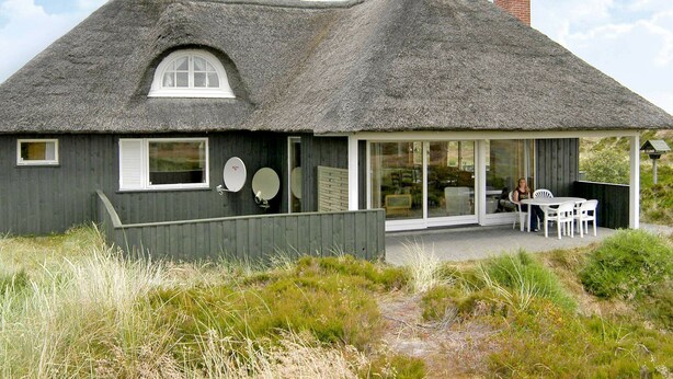 A house with a thatched roof, a large window, and a patio area with outdoor seating. - Cozy Holiday Home in Oksbøl near Beach (Oksbol)