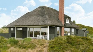 A thatched-roof house with a brick chimney, large windows, and a covered outdoor seating area. - Cozy Holiday Home in Oksbøl near Beach (Oksbol)