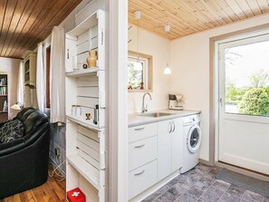 Kompakti keittiö, jossa on valkoiset kaapit, sisäänrakennettu pesukone ja ikkuna, josta avautuu näkymä vehreään maisemaan.