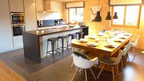 A modern kitchen with a central island, bar stools, and a dining area with a long table set for six. - Cosy apartment in villa for 10 guests with WIFI, TV and balcony (Randogne)