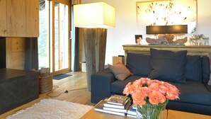 A cozy living room with a sofa, a coffee table with a vase of flowers, and a bookshelf. - Cosy apartment in villa for 10 guests with WIFI, TV and balcony (Randogne)