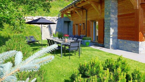A wooden house with a stone exterior, a dining area with outdoor furniture, and a well-maintained lawn. - Cosy apartment in villa for 10 guests with WIFI, TV and balcony (Randogne)