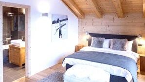 A bedroom with a wooden ceiling, a bed with a grey duvet, a nightstand, a bedside table, and a wall-mounted light. - Cosy apartment in villa for 10 guests with WIFI, TV and balcony (Randogne)