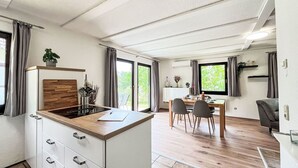 A modern kitchen with a wooden countertop and white cabinets, a dining area with a table and chairs, and large windows offering a view of greenery. - Beautiful apartment in villa for 3 people with WIFI, TV and terrace (Korbach)