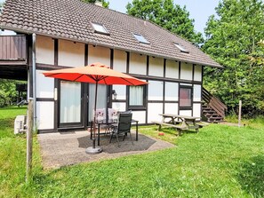Ein zweigeschossiges Haus mit einer Terrassenfläche, inklusive Tisch und Stühlen unter einem roten Sonnenschirm.