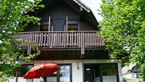 A two-story wooden building with a balcony, a red umbrella, and a table with chairs outside. - Cosy apartment in villa for 4 people with WIFI, A/C, TV, terrace and pets allowed (Bad Wildungen)