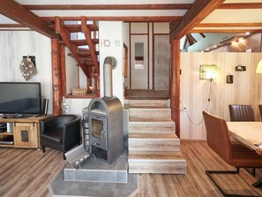 Una sala de estar acogedora con chimenea, televisión y comedor, con suelo de madera y una escalera.