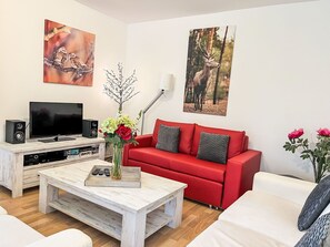Un salon avec un canapé rouge, un divan blanc, une table basse, un téléviseur et un système de haut-parleurs.