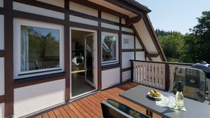 A modern house with a wooden deck, large windows, and a balcony with outdoor seating.