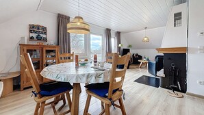 A dining area with a round table, wooden chairs, a hanging light fixture, and a view through a window.