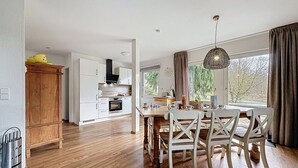 Een moderne keuken met witte kasten, een houten eettafel met stoelen en een groot raam met gordijnen.