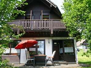 A two-story wooden building with a balcony, a red umbrella, and a table with chairs outside. - Beautiful apartment in villa for 4 people with WIFI, TV, terrace and pets allowed (Bad Wildungen)