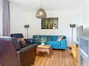Uma sala de estar com sofá, poltrona, mesa de centro, televisão e um quadro na parede.