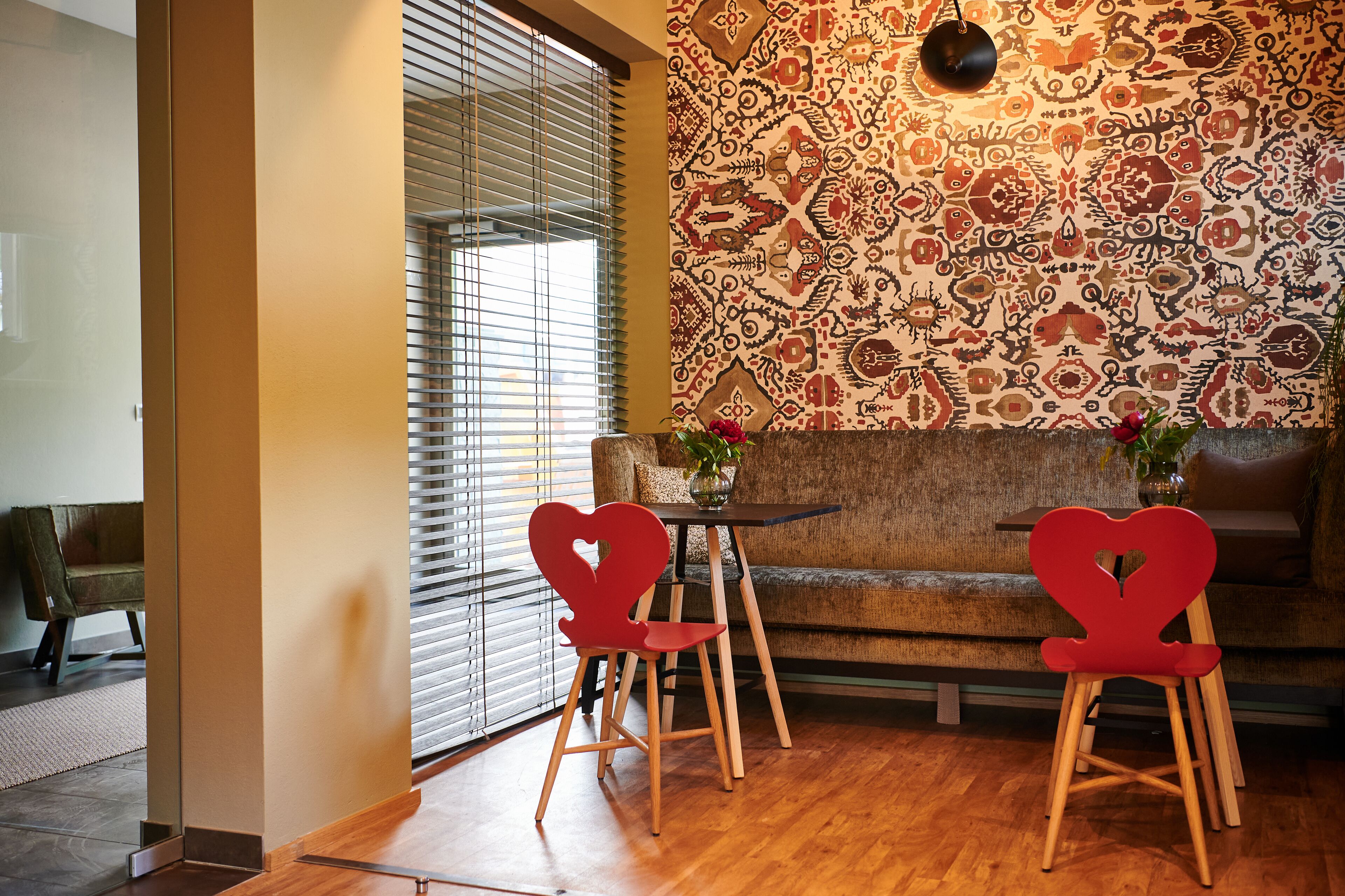 A modern living room with a patterned wall, a wooden floor, and a heart-shaped red chair.