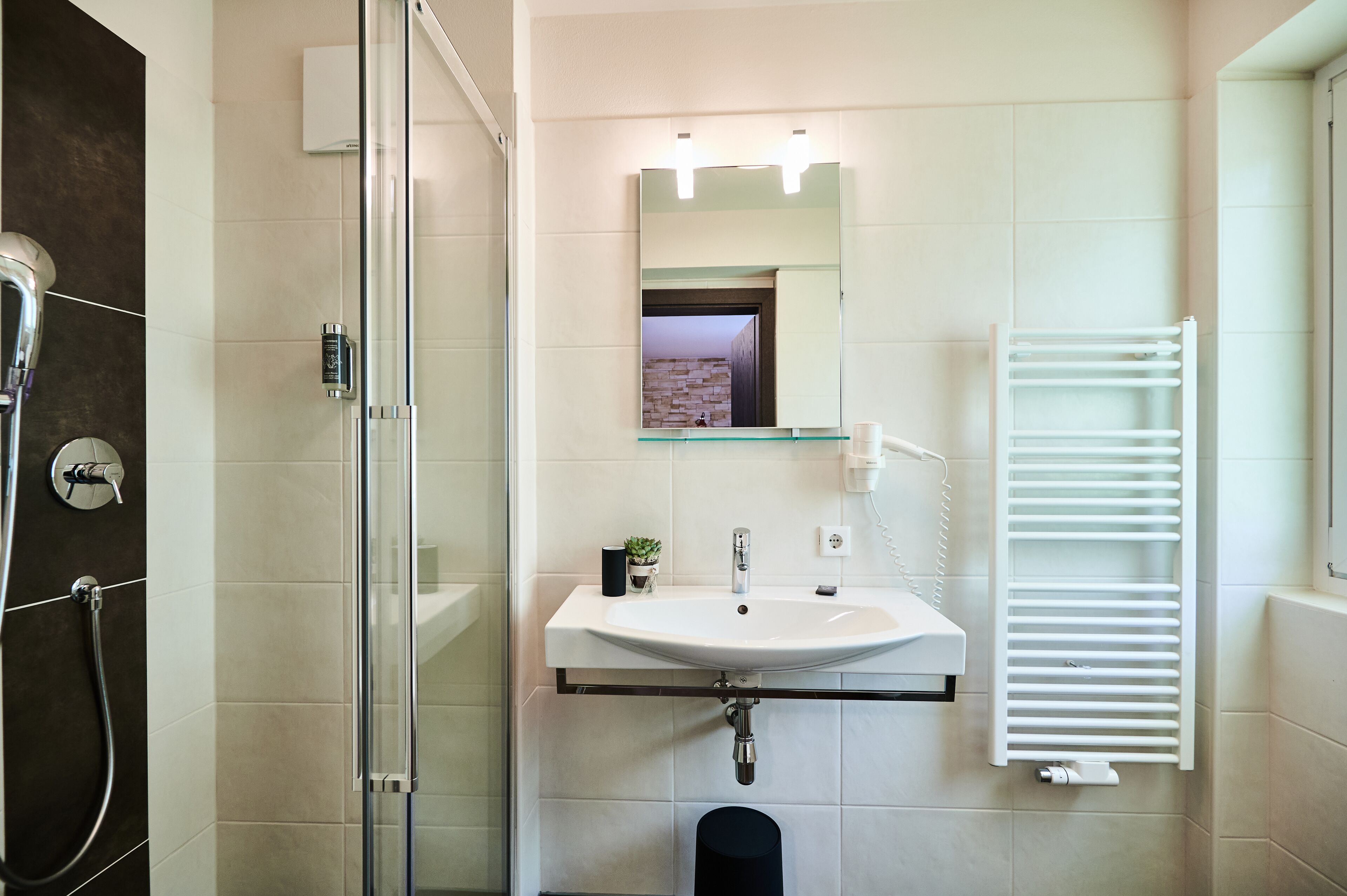 A modern bathroom with a glass shower enclosure, a white sink with a mirror above, and a white towel rack.