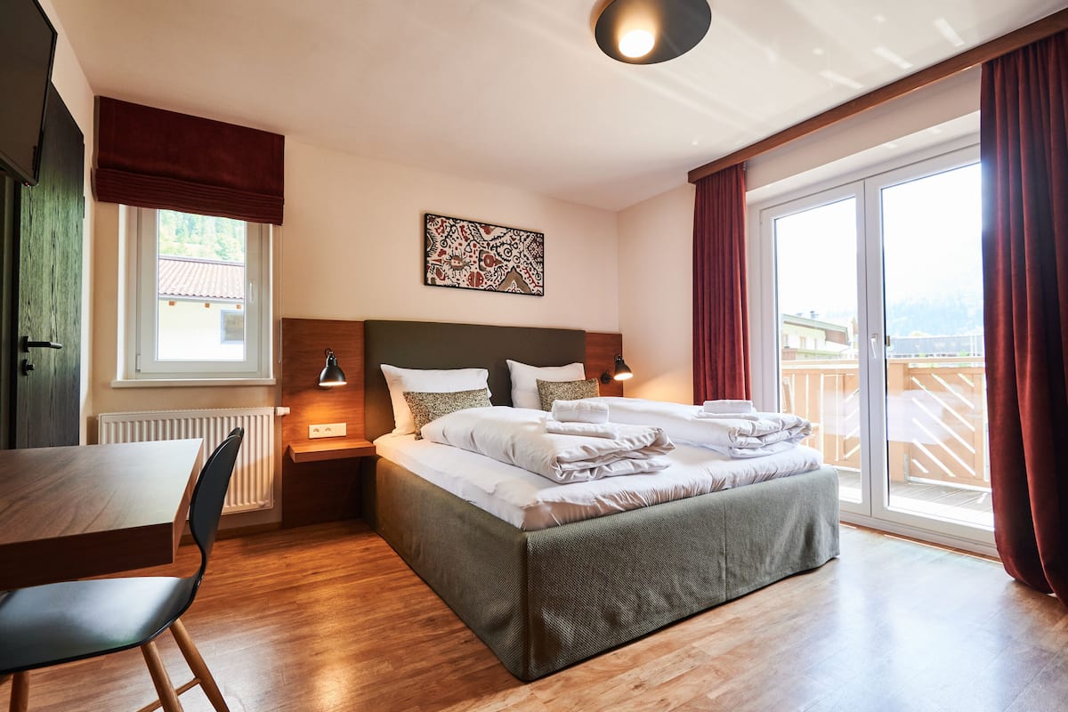 A modern hotel room with a large bed, a dining table, and a view of a wooden deck.