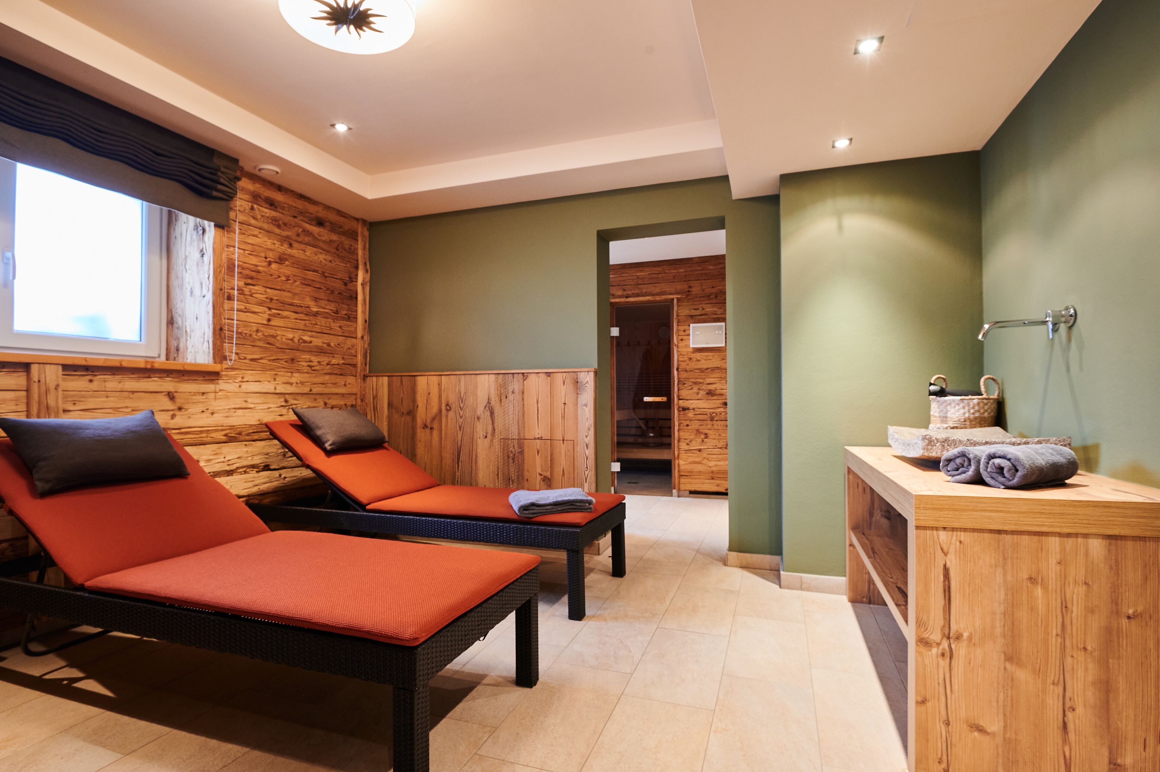 Ein Zimmer mit zwei Lounge-Stühlen, einer Holzkabine mit Handtüchern und Blick auf eine Holzwand sowie eine Tür zu einem anderen Raum.