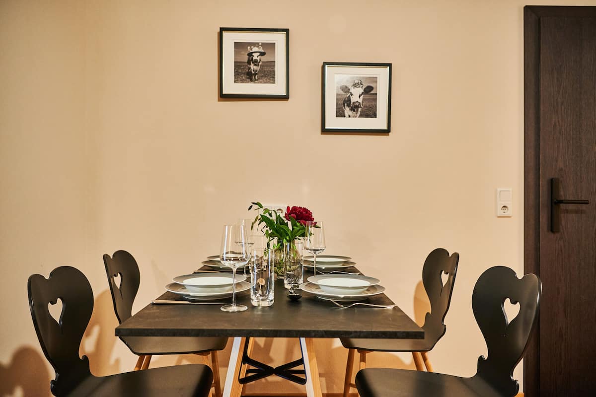 A dining table set for six with chairs, a vase with flowers, and framed pictures on the wall.