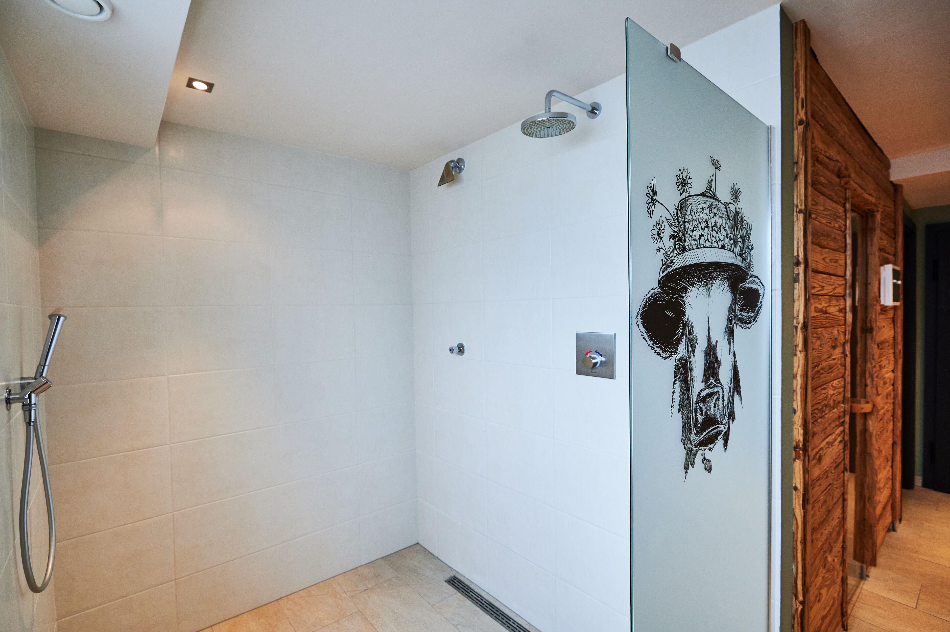 Ein modernes Badezimmer mit weißen Fliesen, einer Duschabtür aus Glas, einer Holzwand und einem dekorativen Wandgemälde.