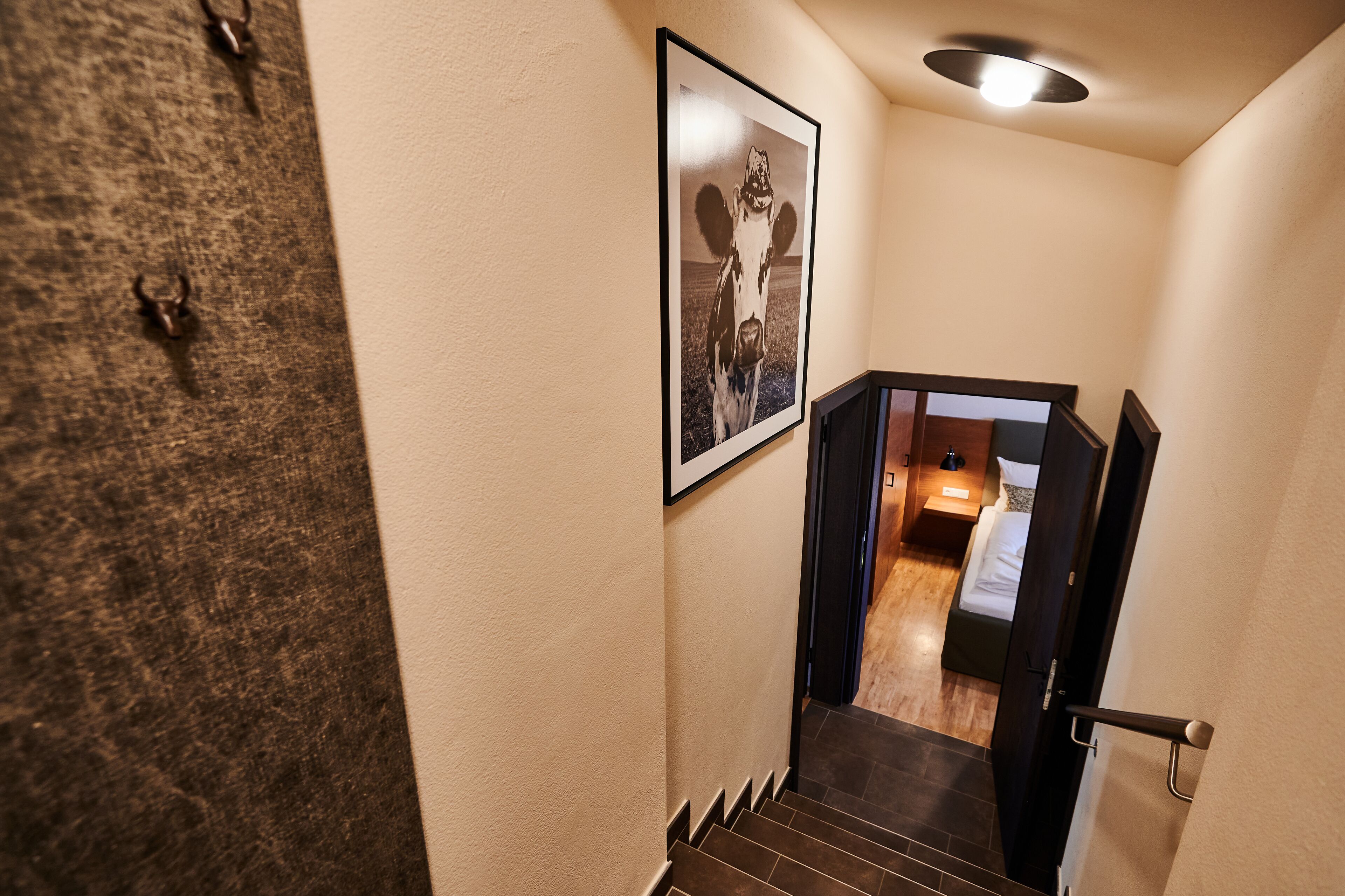 A staircase leading to a bedroom with a bed, a nightstand, and a wall-mounted picture of a cow.