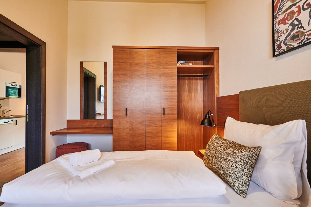 A hotel room with a bed, a wardrobe, a mirror, and a wall-mounted artwork.