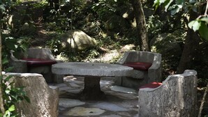 A stone table with four benches, each with a red cushion, surrounded by natural stone flooring and greenery. - Siritamu Resort (Bungoma)