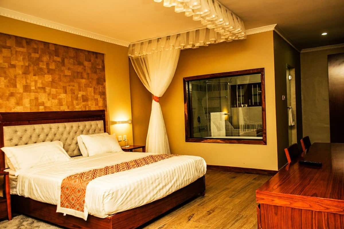 A hotel room with a large bed, a dining table, a window with a view, and a wooden headboard.