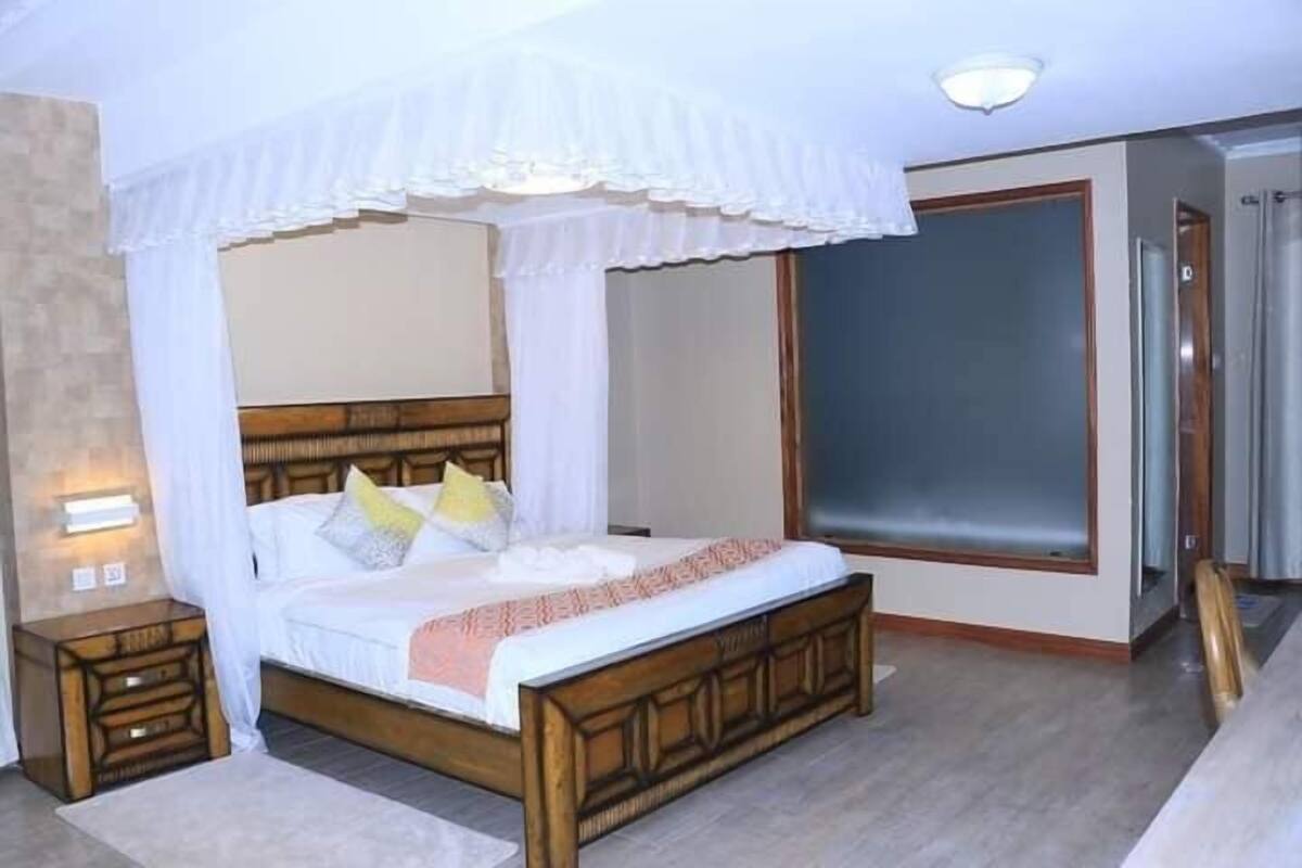 A bedroom with a wooden bed, white curtains, and a nightstand with a lamp.