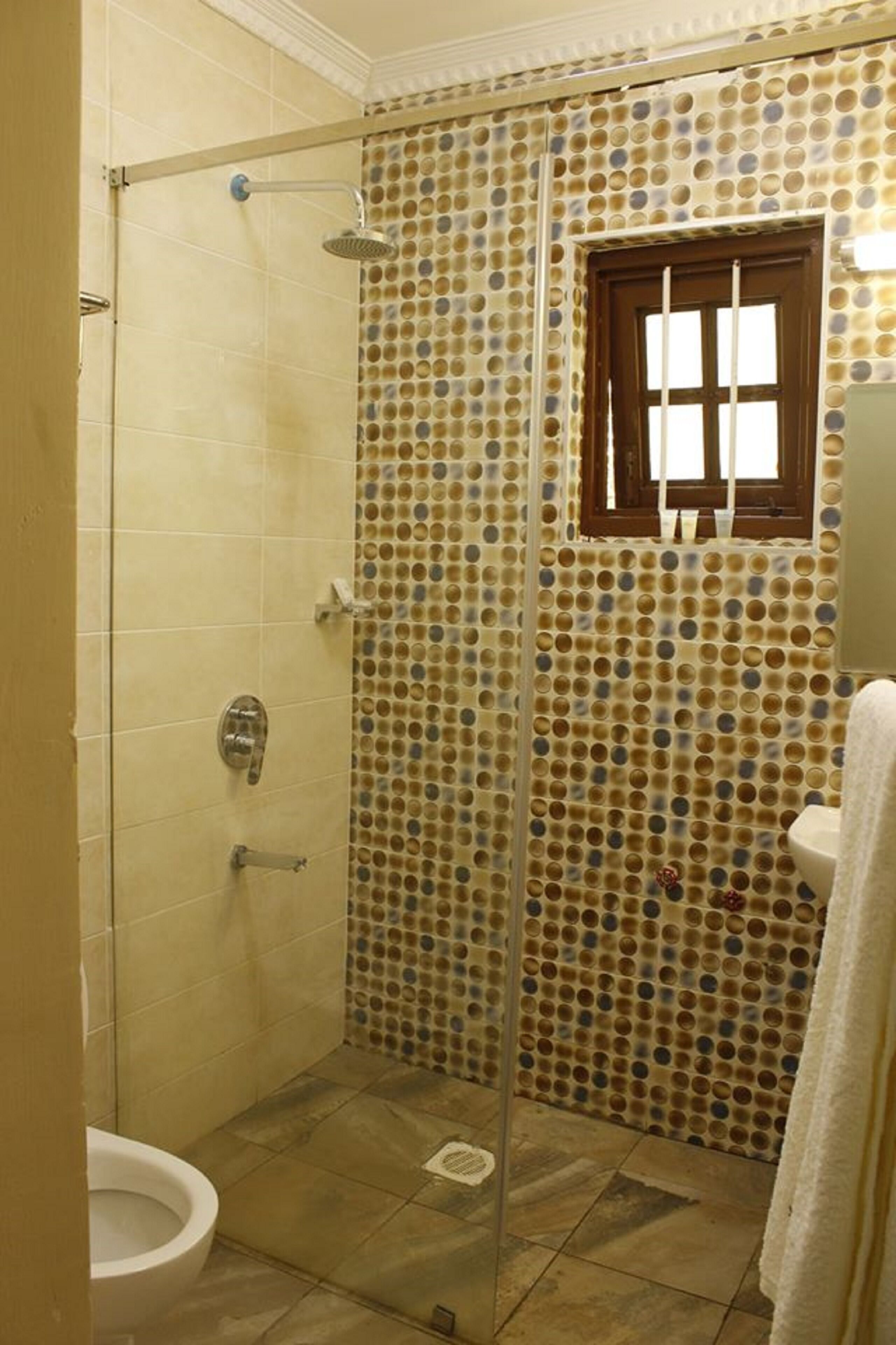 Ein Badezimmer mit Dusche, Toilette und einem Fenster mit Holzrahmen.