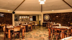 A restaurant with brick walls, wooden tables and chairs, a bar area, and a large mirror on the wall. - Siritamu Resort (Bungoma)