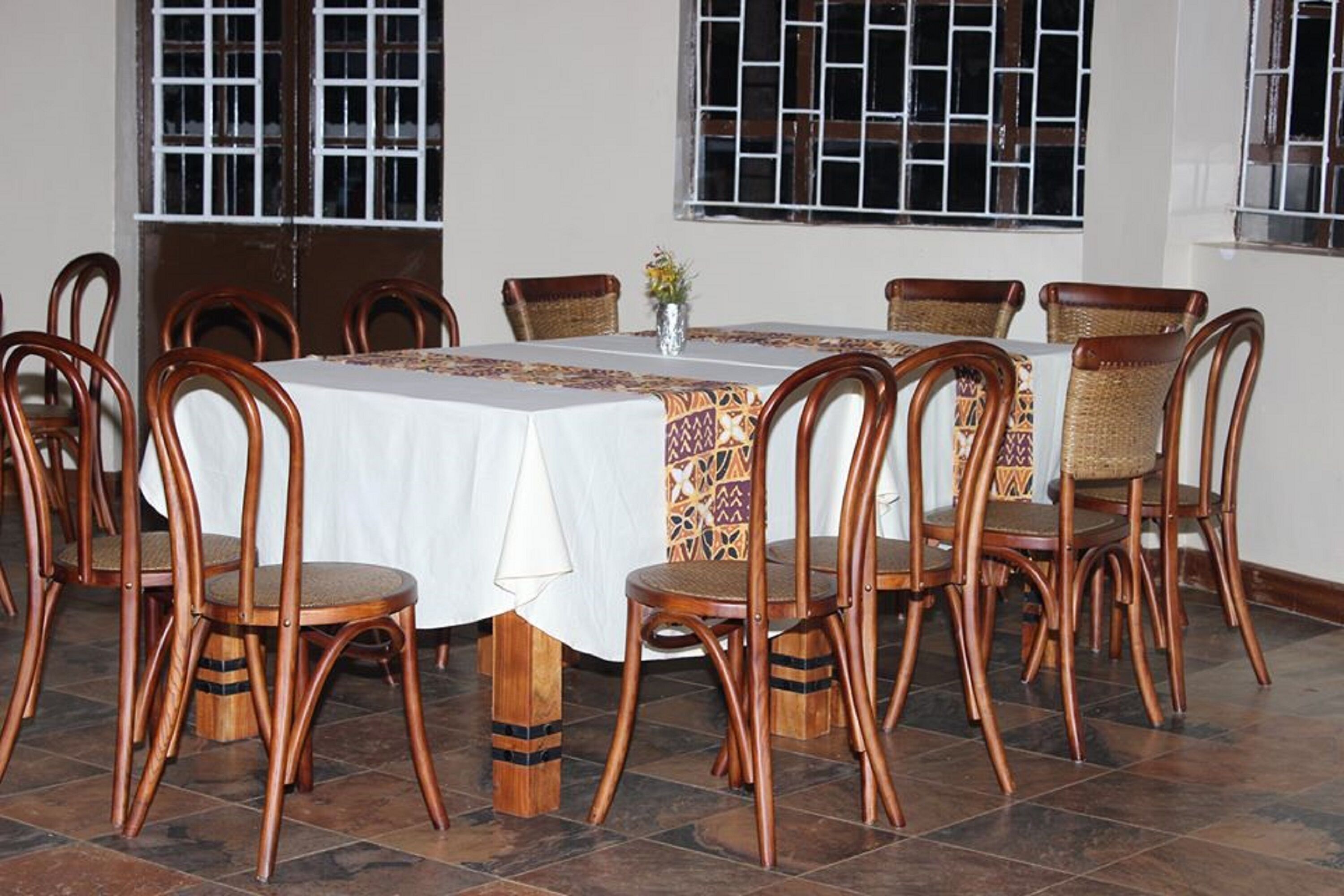 A dining area with a round table covered with a white tablecloth, surrounded by wooden chairs with woven seats.