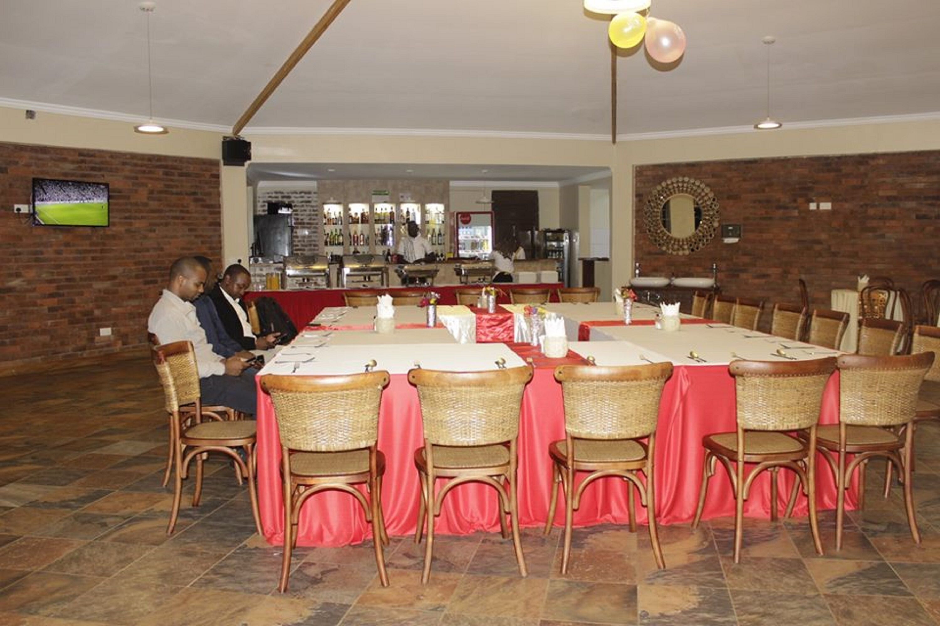 Un restaurante con una larga mesa de comedor, sillas de mimbre y una pared de ladrillo.