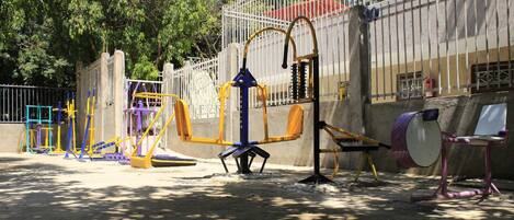 Un parque infantil con varios juegos y equipo de ejercicio, incluyendo columpios, un tobogán y una estructura para escalar.