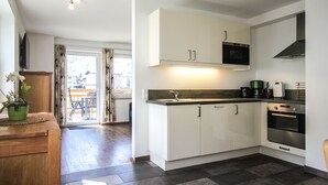 Une cuisine moderne avec des meubles blancs, un four à micro-ondes et un four traditionnel. On y trouve une table à manger en bois, agrémentée d’une plante en pot.
