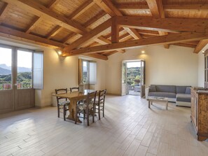 A spacious living area with a wooden ceiling, a dining table with chairs, a sofa, and a view of the outdoors through large windows. - Cosy apartment in villa for 3 guests with pool, WIFI, terrace and pets allowed (Villa Collemandina)