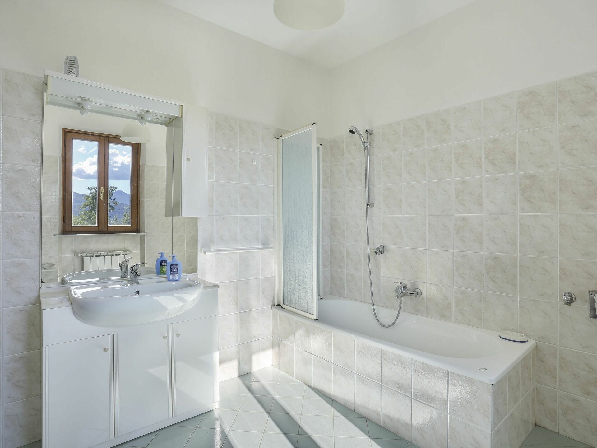 Un bagno con lavandino, specchio e doccia, tutti in bianco.