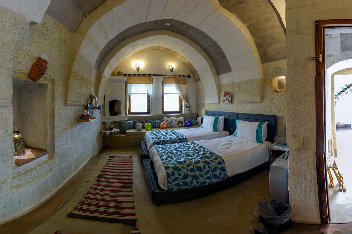Une chambre avec deux lits, une petite fenêtre, une étagère fixée au mur et un plafond en arc de cercle.
