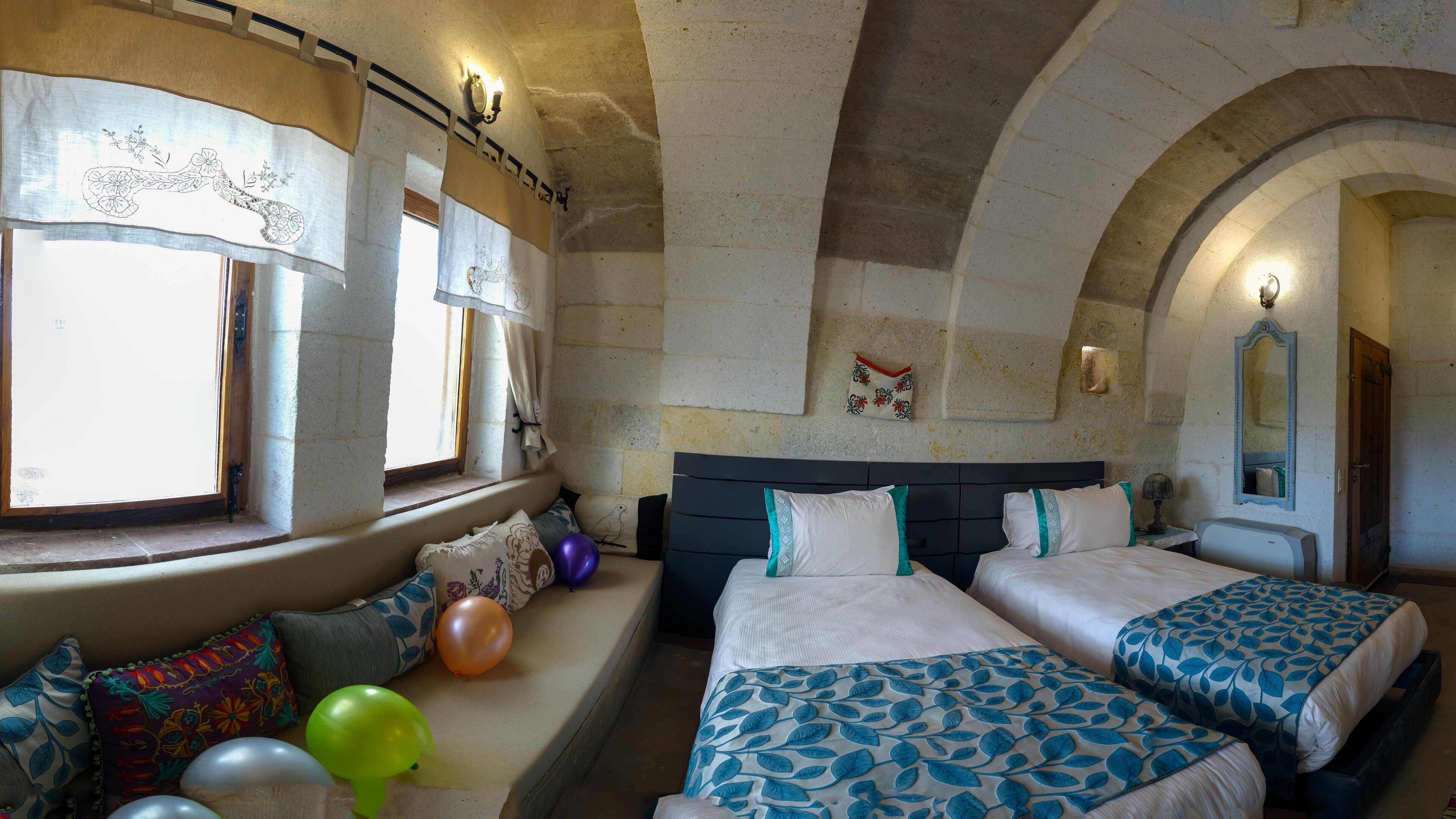 A room with two beds, a bench with balloons, and a stone wall with a window.