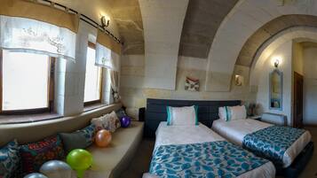 A room with two beds, a bench with balloons, and a stone wall with a window.
