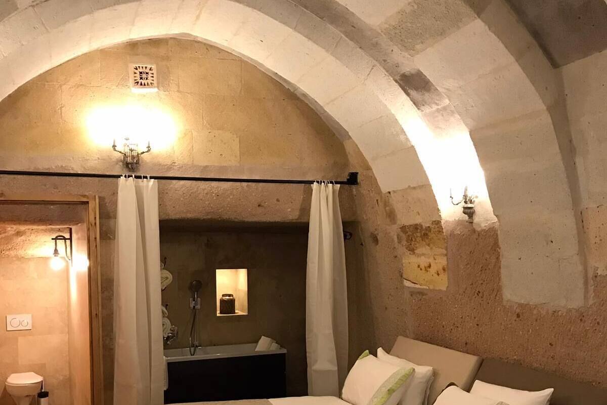Une chambre à coucher avec un plafond en arc de cercle, un lit recouvert de draps blancs, un espace douche et un fauteuil rouge.