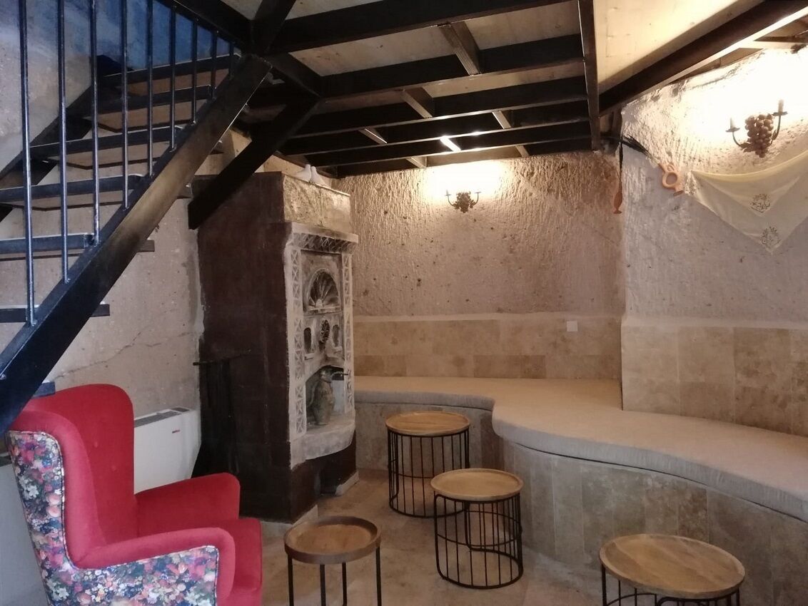 Una habitación con pared de piedra, una silla roja, un banco y una pequeña mesa.