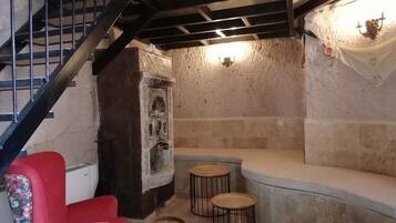 Una habitación con pared de piedra, una silla roja, un banco y una pequeña mesa.
