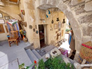 Un interior rústico de piedra con una silla de madera, una cama y varios objetos decorativos.